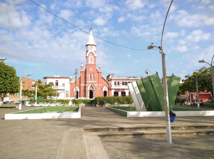 Plaza pavimentada del Parque Obrero de Puerto Berrío, con jardineras y paneles verdes y una iglesia al fondo.